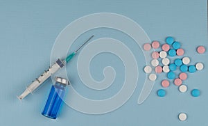 Medical syringe and colorful pills on a blue background. choose between vaccination and treatment