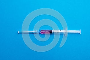 Medical syringe filled with pink liquid isolated on a blue background close-up. The view from the top. Concepts of medicine.