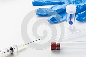 Medical syringe, glass tubes, stool test sampler and blue latex glove on white