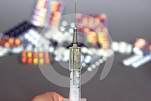 Medical syringe in hand with a needle and colorful pills capsule on background