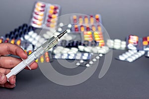 Medical syringe in hand with a needle and colorful pills capsule on background