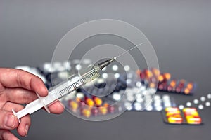 Medical syringe in hand with a needle and colorful pills capsule on background