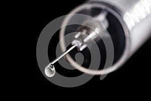 Medical syringe, injection with focus on the needle, falling drop, dripping liquid, macro photography, spot focus. Concept of cure