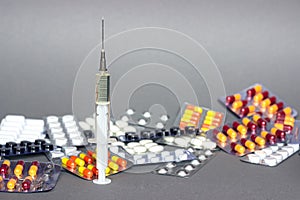Medical syringe with a needle and colorful pills capsule on background