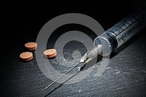 Medical syringe with needle and pills on dark background in low light