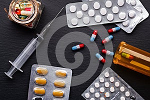 Medical syringe with needle and pills on dark background. View from above