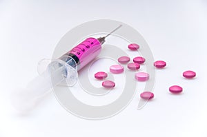 A medical syringe with a purple solution lies on a white background surrounded by pills