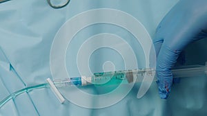 Medical syringe pushes blue liquid into IV tubing or catheter over blue sheet