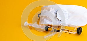 Medical syringe and white respirator on a yellow background