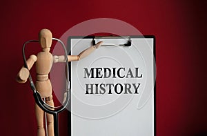 Medical table with a wooden person along with a stethoscope. Inscription MEDICAL HISTORY on the clipboard with the holder. Health