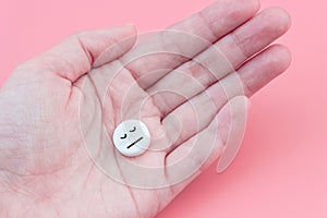 Medical tablet with a sleeping smiley in hand on a pink background. Sleeping pills for insomnia
