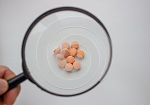 Medical tablets under a magnifying glass on a white background.