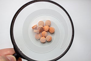 Medical tablets under a magnifying glass on a white background.