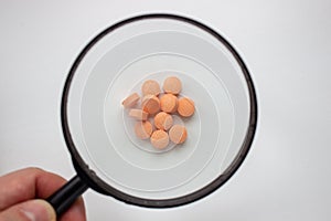 Medical tablets under a magnifying glass on a white background.