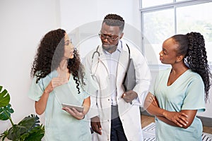 Medical team discuss patient case while standing looking serious, doctor nurses