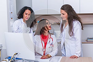 Medical Team  Female doctor  medic  in her 30`s working on her computer while two female nurses stand next to her and discus