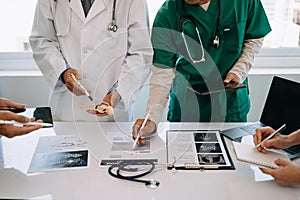 Medical team having a meeting with doctors in white lab coats and surgical scrubs seated at a desk discussing a patients working