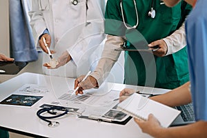 Medical team having a meeting with doctors in white lab coats and surgical scrubs seated at a desk discussing a patients working