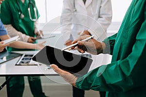 Medical team having a meeting with doctors in white lab coats and surgical scrubs seated at a desk discussing a patients working