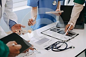 Medical team having a meeting with doctors in white lab coats and surgical scrubs seated at a desk discussing a patients working