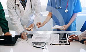 Medical team having a meeting with doctors in white lab coats and surgical scrubs seated at a desk discussing a patients working