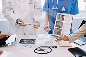 Medical team having a meeting with doctors in white lab coats and surgical scrubs seated at a desk discussing a patients working
