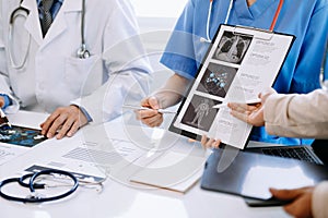 Medical team having a meeting with doctors in white lab coats and surgical scrubs seated at a desk discussing a patients working