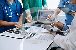 Medical team having a meeting with doctors in white lab coats and surgical scrubs seated at a table discussing a patients working