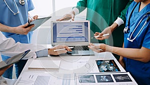 Medical team having a meeting with doctors in white lab coats and surgical scrubs seated at a table discussing a patients working