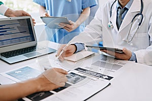 Medical team having a meeting with doctors in white lab coats and surgical scrubs seated at a table discussing a patients working