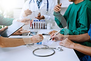 Medical team having a meeting with doctors in white lab coats and surgical scrubs seated at a table discussing a patients working