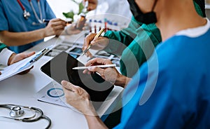 Medical team having a meeting with doctors in white lab coats and surgical scrubs seated at a table discussing a patients working