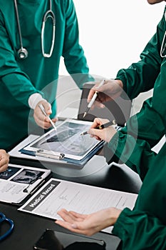 Medical team having a meeting with doctors in white lab coats and surgical scrubs seated at a table discussing a patients working