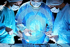 Medical team performing operation. Group of surgeon at work in operating theatre toned in blue