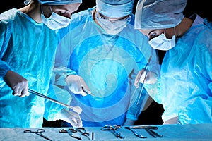 Medical team performing operation. Group of surgeon at work in operating theatre toned in blue