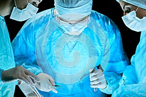 Medical team performing operation. Group of surgeon at work in operating theatre toned in blue