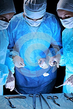 Medical team performing operation. Group of surgeon at work in operating theatre toned in blue