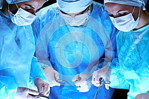 Medical team performing operation. Group of surgeon at work in operating theatre toned in blue