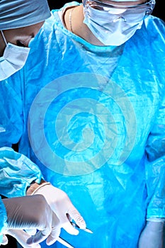 Medical team performing operation. Group of surgeon at work in operating theatre toned in blue