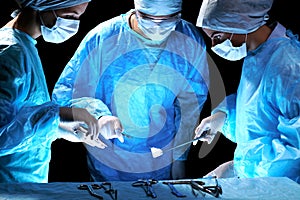 Medical team performing operation. Group of surgeon at work in operating theatre toned in blue