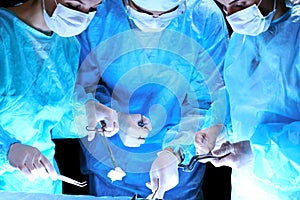 Medical team performing operation. Group of surgeon at work in operating theatre toned in blue