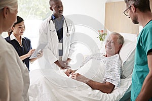 Medical Team On Rounds Meeting Around Bed Of Senior Male Patient