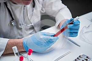 A medical test tube in the hands of a laboratory chemist wearing medical gloves. The desktop of a laboratory assistant