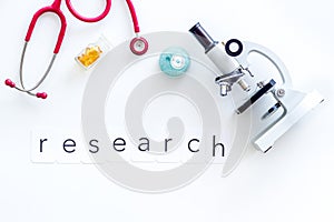 Medical tests on work desk of doctor with microscope, stethoscope, test tube and word research white background top view