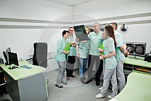 Medical theme.Observation room with a computer tomograph. The group of doctors meeting in the mri office and looking at x-ray at