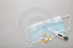 Medical thermometer and mask with pills on grey. Medical concept with copy space