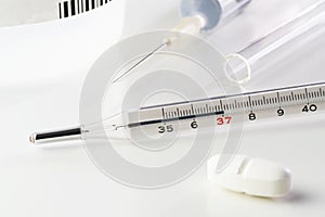 Medical thermometer, pill, vaccine in medical syringe and glass tube on white