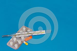 Medical thermometer with pills on on a blue background