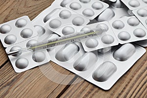 Medical thermometer and tablets in silvery blisters on a wooden table