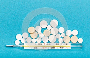 Medical  thermometer and white pills on blue  background close up view